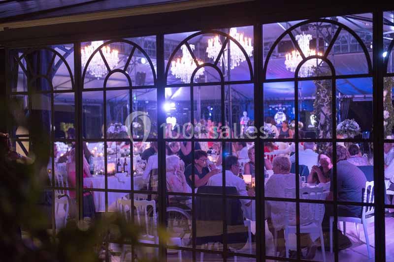 Vue à travers des fenêtres d'une salle éclairée, avec des invités assis à des tables lors d'un événement festif.