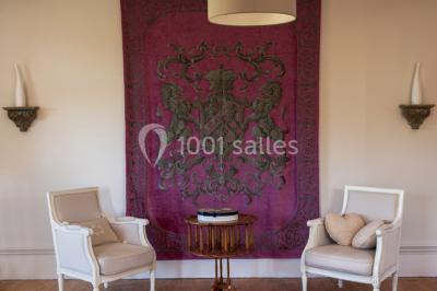 Commode rouge surmontée de cadres, lampe noire et carafe, avec un mur en pierre en arrière-plan.