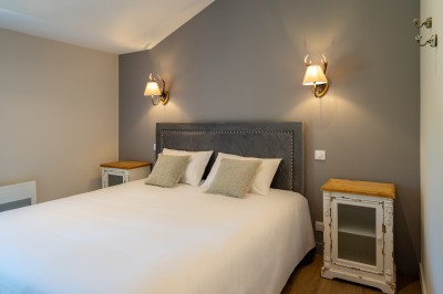 Commode rouge surmontée de cadres, lampe noire et carafe, avec un mur en pierre en arrière-plan.