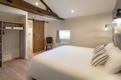 Commode rouge surmontée de cadres, lampe noire et carafe, avec un mur en pierre en arrière-plan.