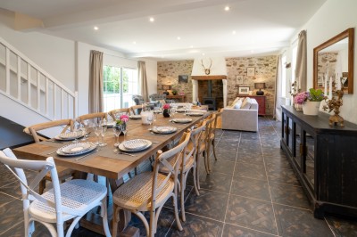 Commode rouge surmontée de cadres, lampe noire et carafe, avec un mur en pierre en arrière-plan.