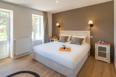 Commode rouge surmontée de cadres, lampe noire et carafe, avec un mur en pierre en arrière-plan.