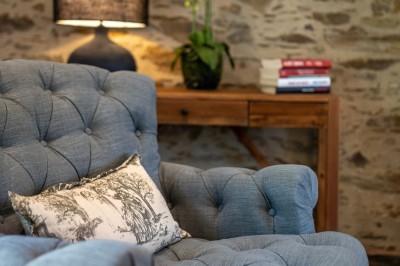 Commode rouge surmontée de cadres, lampe noire et carafe, avec un mur en pierre en arrière-plan.