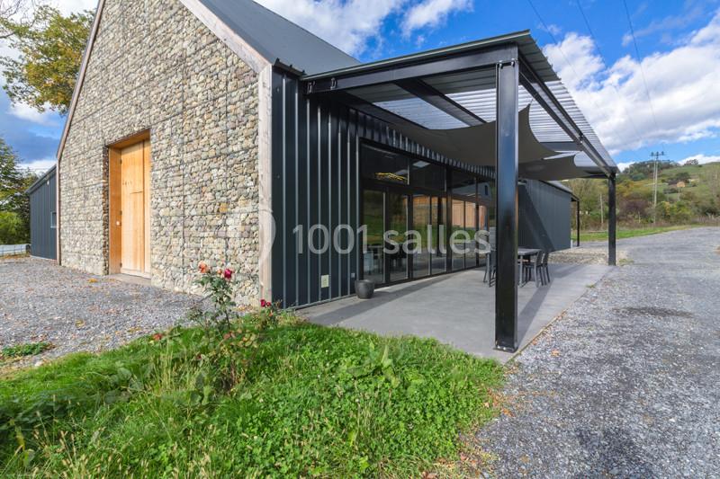 Bâtiment moderne avec façade en pierre et métal, terrasse couverte et environnement rural.