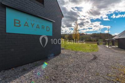 Une femme en robe de mariée sourit face à un homme en costume orange dans un vignoble verdoyant.