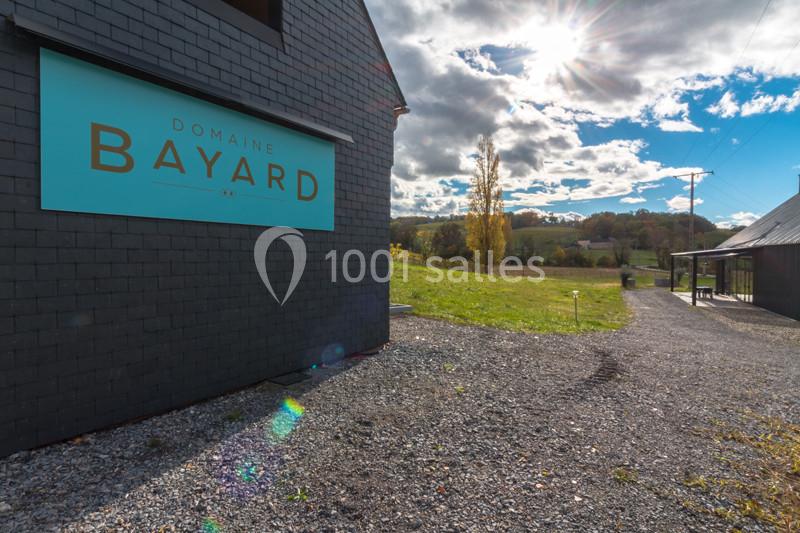 Bâtiment avec une enseigne ’Domaine Bayard’ entouré d'un paysage rural sous un ciel partiellement ensoleillé.