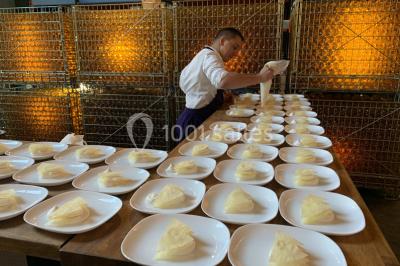 Une femme en robe de mariée sourit face à un homme en costume orange dans un vignoble verdoyant.
