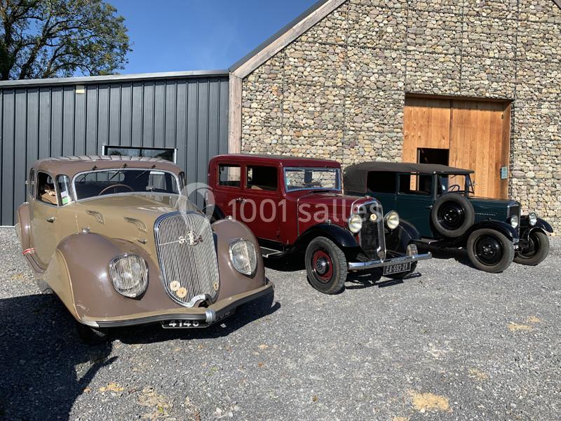 Trois voitures anciennes stationnées devant un bâtiment en pierre sous un ciel dégagé.