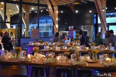 Une femme en robe de mariée sourit face à un homme en costume orange dans un vignoble verdoyant.