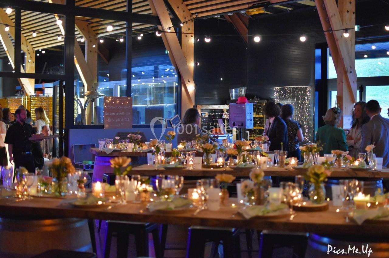 Salle décorée pour un événement, avec tables ornées de fleurs et bougies, et invités discutant debout.