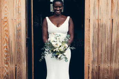 Une femme en robe de mariée sourit face à un homme en costume orange dans un vignoble verdoyant.