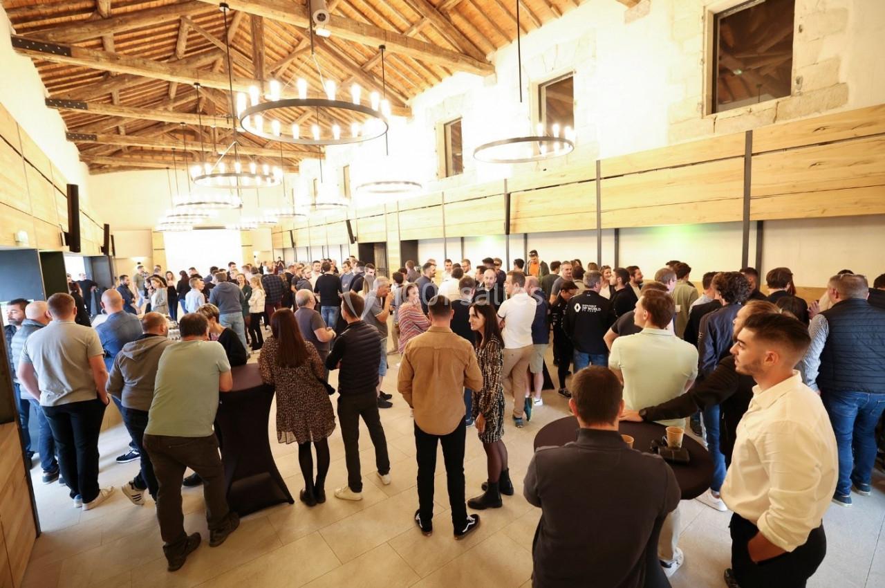 Groupe de personnes échangeant dans une grande salle lumineuse avec plafond en bois et lustres circulaires.