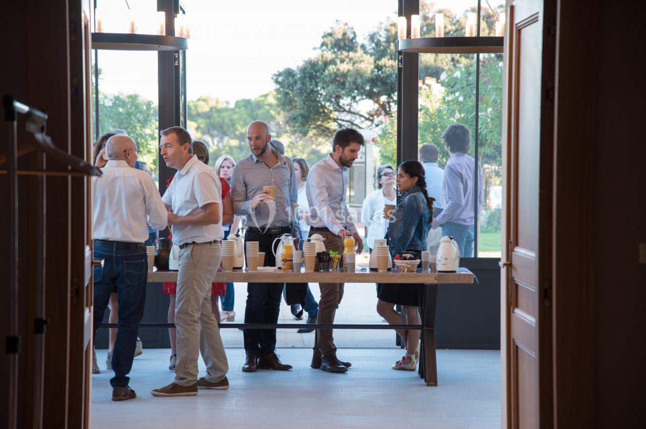 Des personnes discutent autour d'une table avec des boissons dans une salle lumineuse donnant sur un espace extérieur.