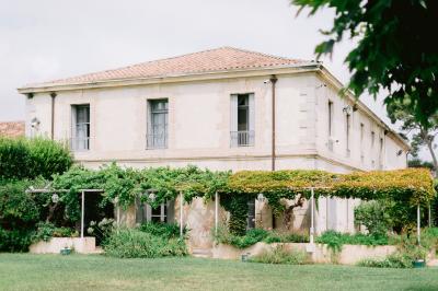 Façade d'une maison en pierre avec toit en tuiles, entourée de végétation dense sous une lumière douce.