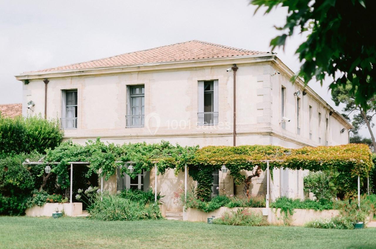 Grande maison en pierre avec toit en tuiles, entourée de verdure et d'une pergola couverte de plantes grimpantes.