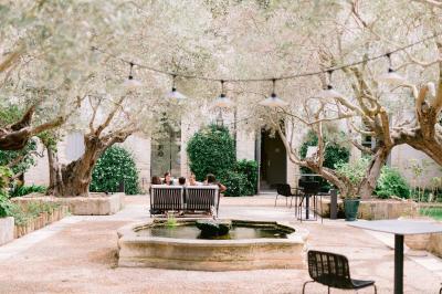 Façade d'une maison en pierre avec toit en tuiles, entourée de végétation dense sous une lumière douce.
