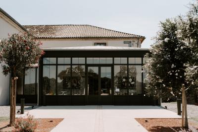 Façade d'une maison en pierre avec toit en tuiles, entourée de végétation dense sous une lumière douce.