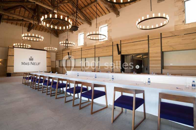 Salle de réunion spacieuse avec une longue table, chaises en bois, éclairage suspendu et écran de projection.