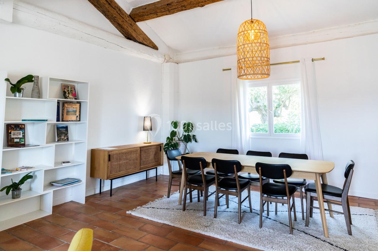 Salle à manger lumineuse avec table en bois, chaises noires, étagère blanche, suspension en osier et fenêtre donnant sur un…
