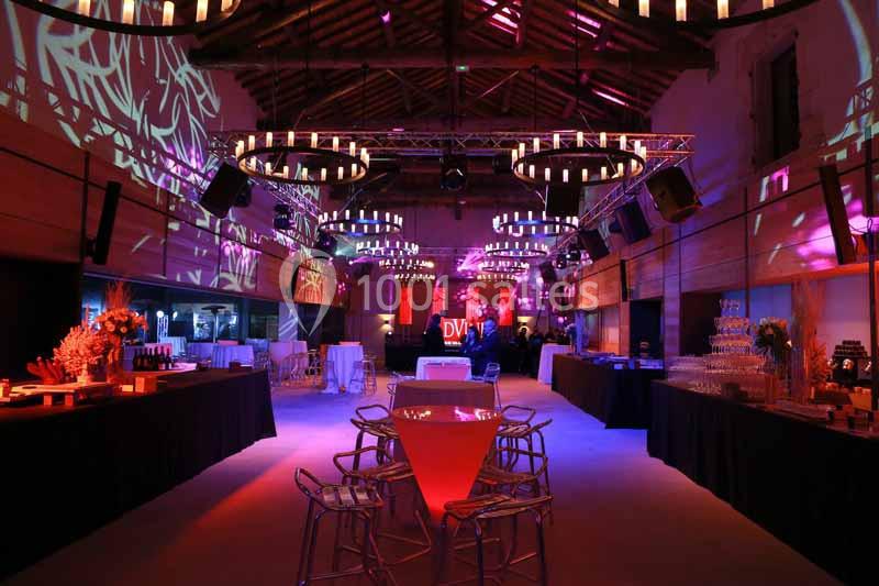 Salle de réception décorée avec des jeux de lumière colorés, tables hautes et buffets aménagés.