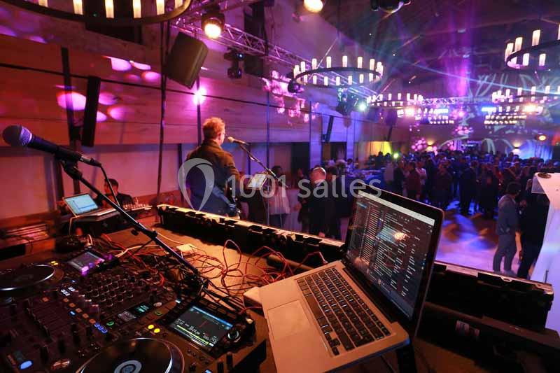 Vue d'une scène de concert avec un DJ en premier plan et une salle éclairée remplie de participants en arrière-plan.