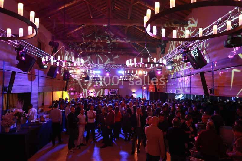 Salle événementielle remplie de personnes, éclairée par des lumières colorées et des lustres suspendus.