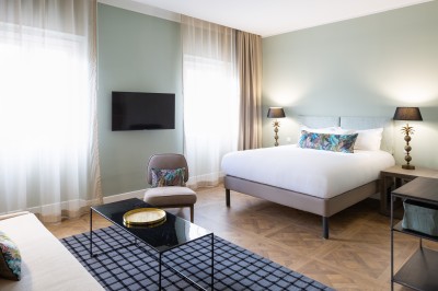 Chambre lumineuse avec lit double, canapé, fauteuils, table ronde et décoration murale dans un intérieur aux tons jaunes.