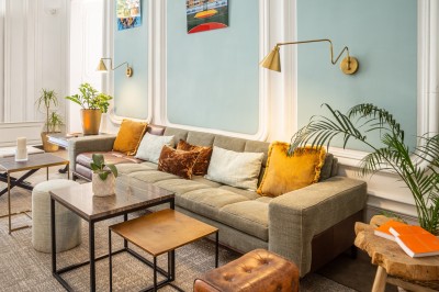 Chambre lumineuse avec lit double, canapé, fauteuils, table ronde et décoration murale dans un intérieur aux tons jaunes.