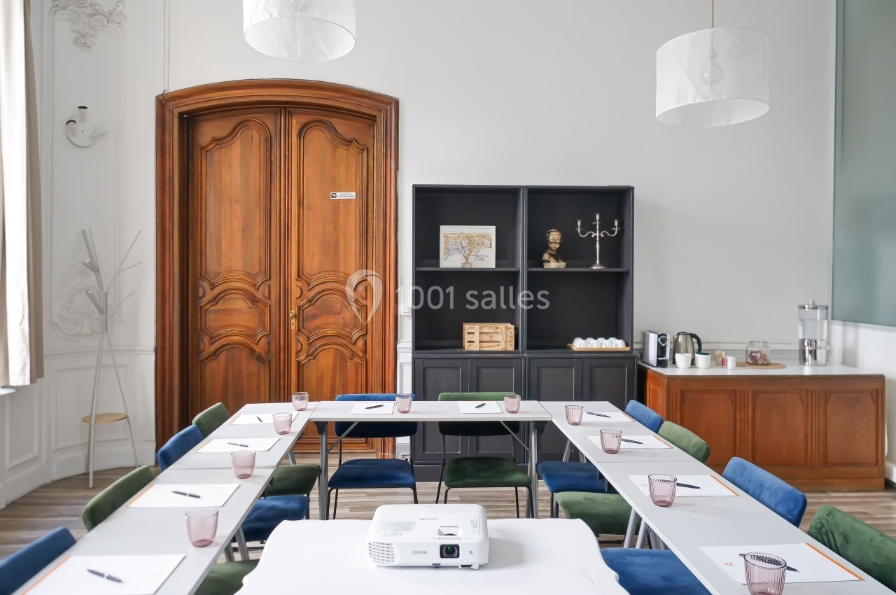 Salle de réunion lumineuse avec table en U, chaises colorées, rétroprojecteur et buffet en arrière-plan.