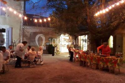 Salle décorée pour un événement, avec des tables alignées, nappes blanches, chemins de table rouges et lanternes suspendues.