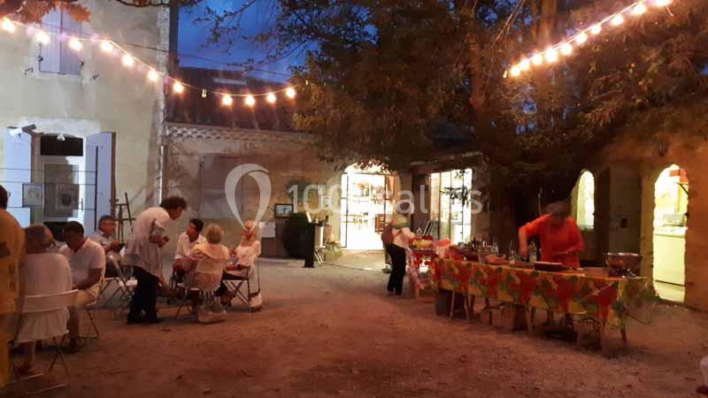 Cour extérieure éclairée par des guirlandes, avec des personnes dînant à des tables et un buffet en préparation.