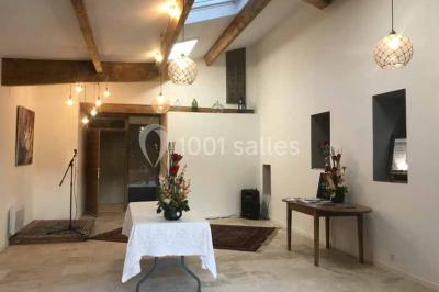 Salle décorée pour un événement, avec des tables alignées, nappes blanches, chemins de table rouges et lanternes suspendues.