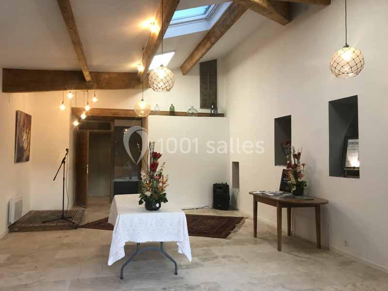 Salle lumineuse avec poutres apparentes, tables décorées de fleurs et éclairage suspendu.