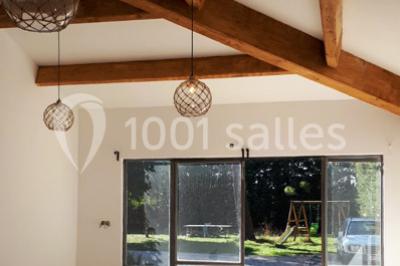 Salle décorée pour un événement, avec des tables alignées, nappes blanches, chemins de table rouges et lanternes suspendues.