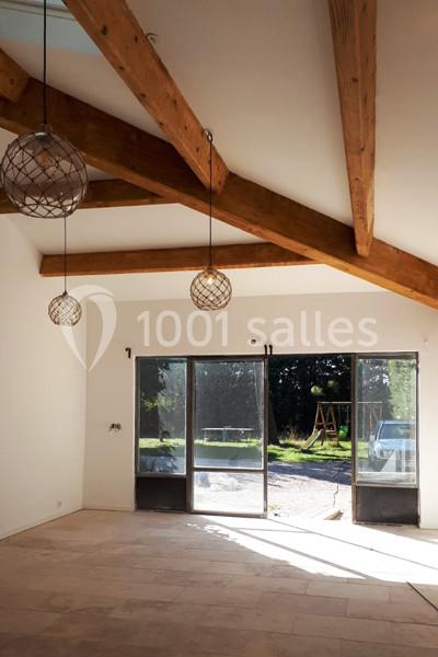 Intérieur lumineux avec poutres apparentes, grandes baies vitrées donnant sur un jardin avec balançoire.