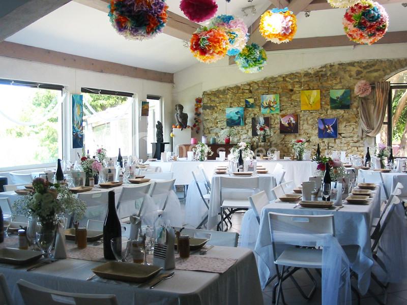 Salle de réception décorée avec des tables dressées, des fleurs, des guirlandes colorées et des tableaux au mur.