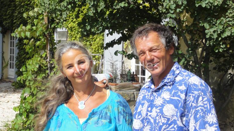 Un homme et une femme sourient devant une maison entourée de végétation.