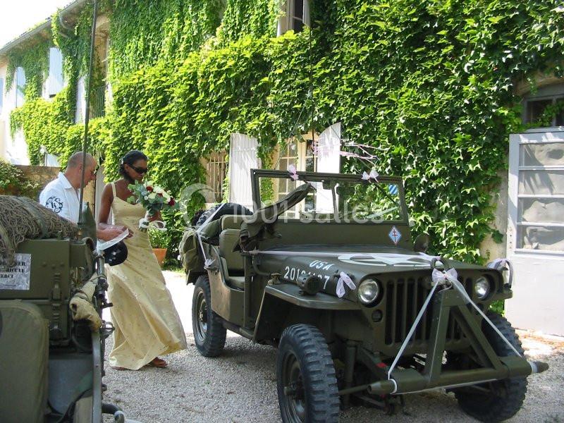 Une mariée monte dans une jeep militaire décorée, devant un bâtiment couvert de lierre.