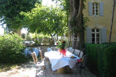 Salle décorée pour un événement, avec des tables alignées, nappes blanches, chemins de table rouges et lanternes suspendues.