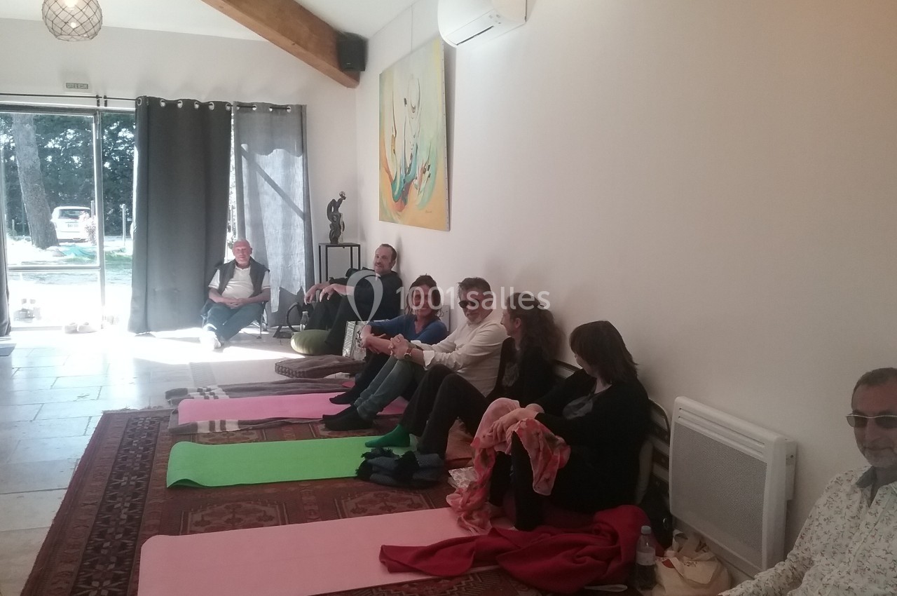 Des personnes assises sur des tapis et des chaises dans une salle lumineuse avec des œuvres d'art au mur.