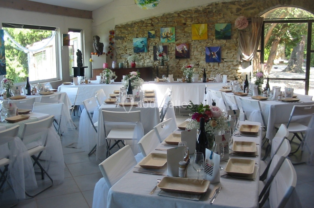 Salle de réception décorée avec des tables dressées, nappes blanches, chaises pliantes et ornements colorés.