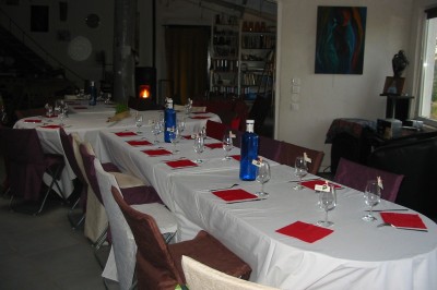 Salle décorée pour un événement, avec des tables alignées, nappes blanches, chemins de table rouges et lanternes suspendues.