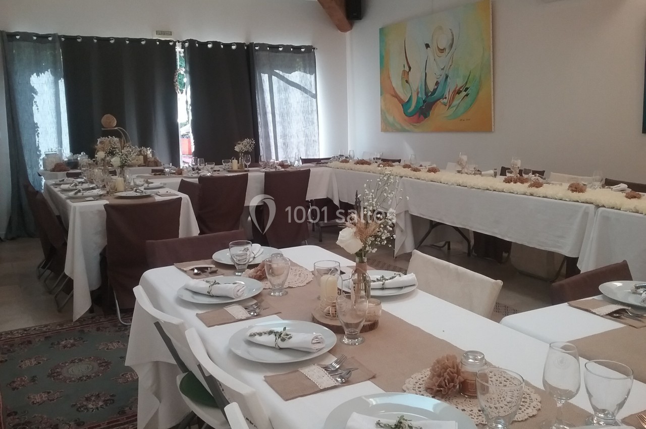 Salle décorée pour un repas festif avec tables dressées, nappes blanches, chemins de table en lin et décorations florales.