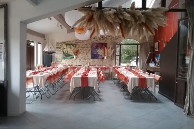 Salle décorée pour un événement, avec des tables alignées, nappes blanches, chemins de table rouges et lanternes suspendues.