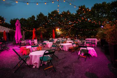 Miniature Cabaret Sauvage - Extérieur Terrasse extérieure avec tables rondes, chaises pliantes et guirlandes lumineuses suspendues, ambiance en soirée.