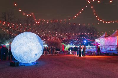 Miniature Cabaret Sauvage - Extérieur Terrasse extérieure avec tables rondes, chaises pliantes et guirlandes lumineuses suspendues, ambiance en soirée.