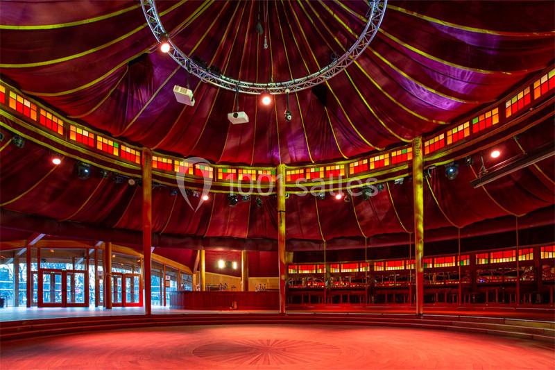 Intérieur d'un chapiteau circulaire avec une structure en bois, éclairage chaleureux et rideaux rouges.