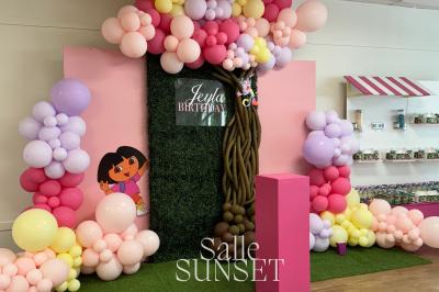 Décoration d'anniversaire avec ballons colorés, fond végétal, et personnages de dessin animé dans une salle festive.