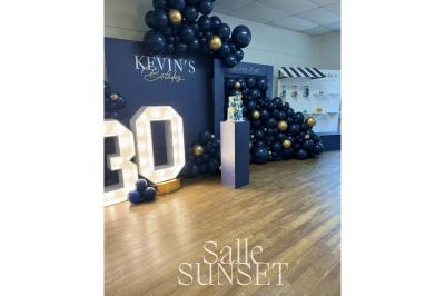 Décoration d'anniversaire avec ballons colorés, fond végétal, et personnages de dessin animé dans une salle festive.