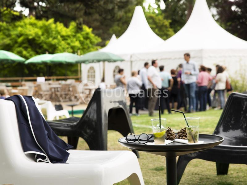 Des chaises et une table avec des boissons en extérieur, devant des tentes blanches et un groupe de personnes.